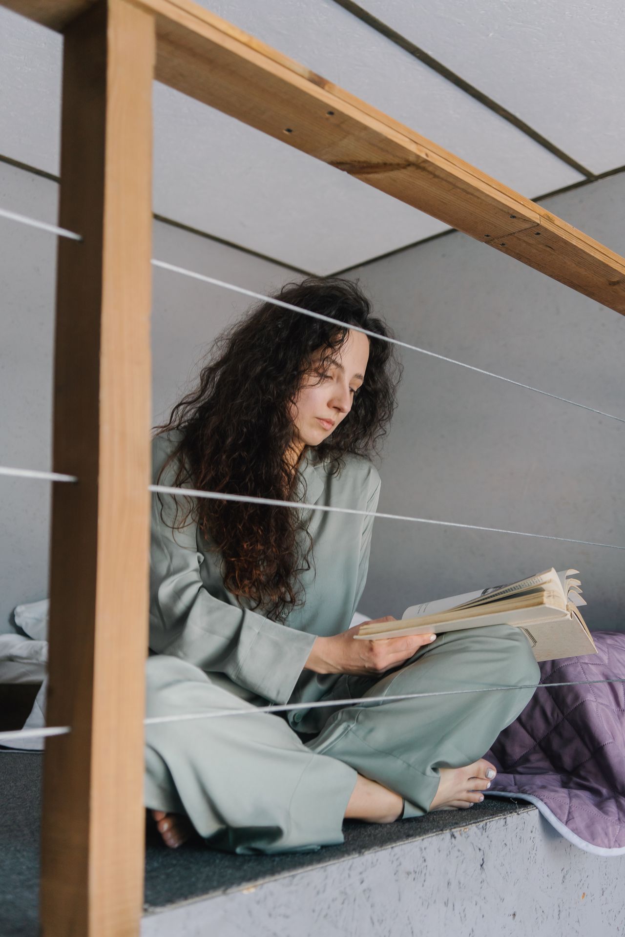 Woman in a sage green pajama set reading on a loft bed