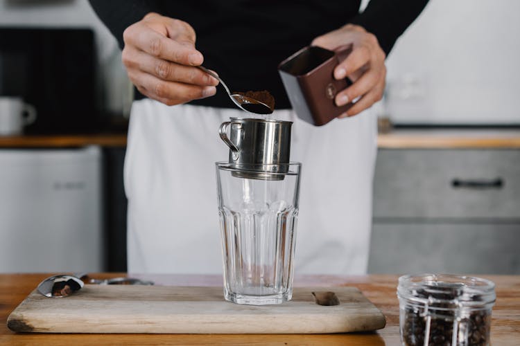 Person Putting A Scoop Of Ground Coffee On A Metal Cup