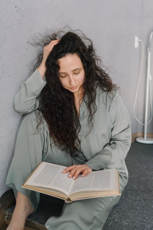 Free A woman with curly hair relaxes indoors, reading a book in a cozy home environment. Stock Photo