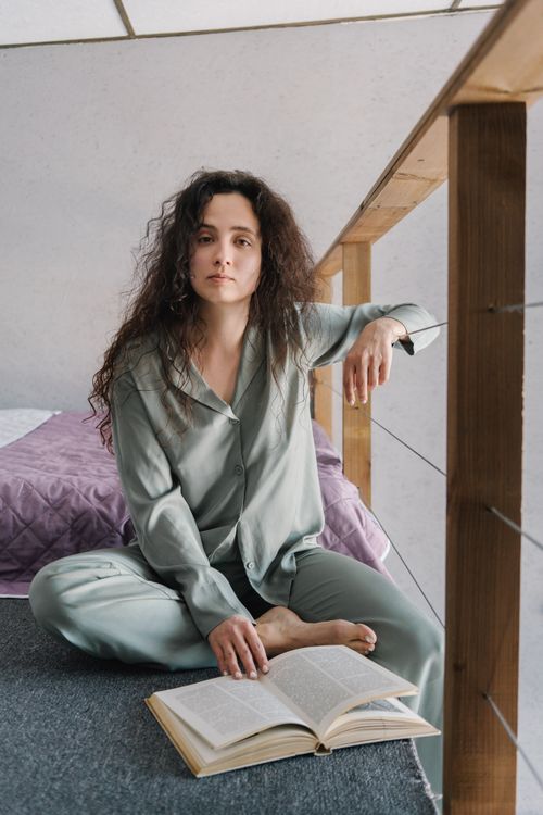 Free A woman in pajamas seated reading a book in a cozy indoor setting, reflecting relaxation and tranquility. Stock Photo
