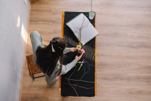 Free A woman creatively arranging flowers in a vase on a wooden table from a high angle view. Stock Photo
