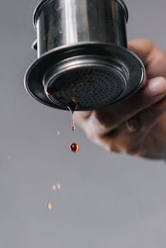 Detailed view of a hand holding a dripping coffee strainer, highlighting the brewing process.