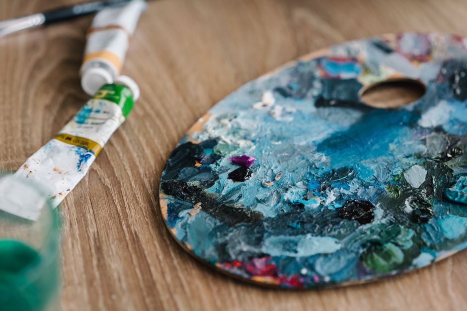 Close-up of an artist's messy palette with vibrant paint tubes on wooden surface.