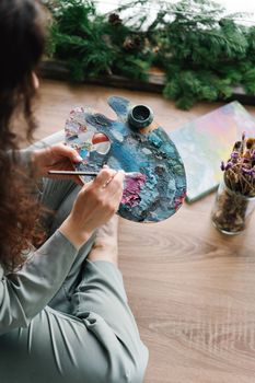 Woman artist painting with palette and brushes indoors, creative atmosphere.