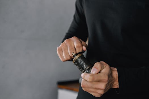 Close-up view of hands in black shirt operating an ornate vintage weed grinder indoors.
