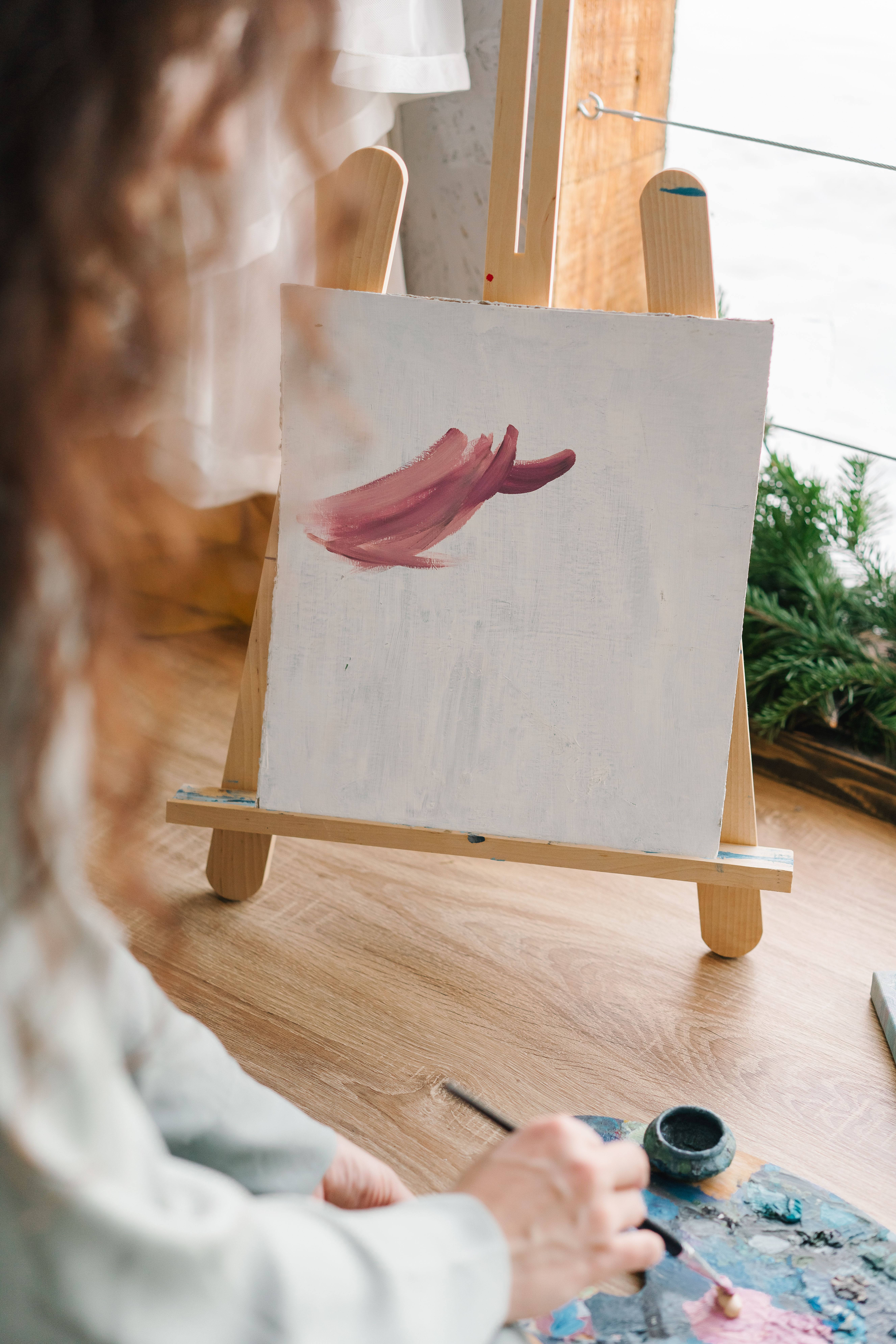 Artist begins a painting in a bright, cozy studio using pink brush strokes on canvas.