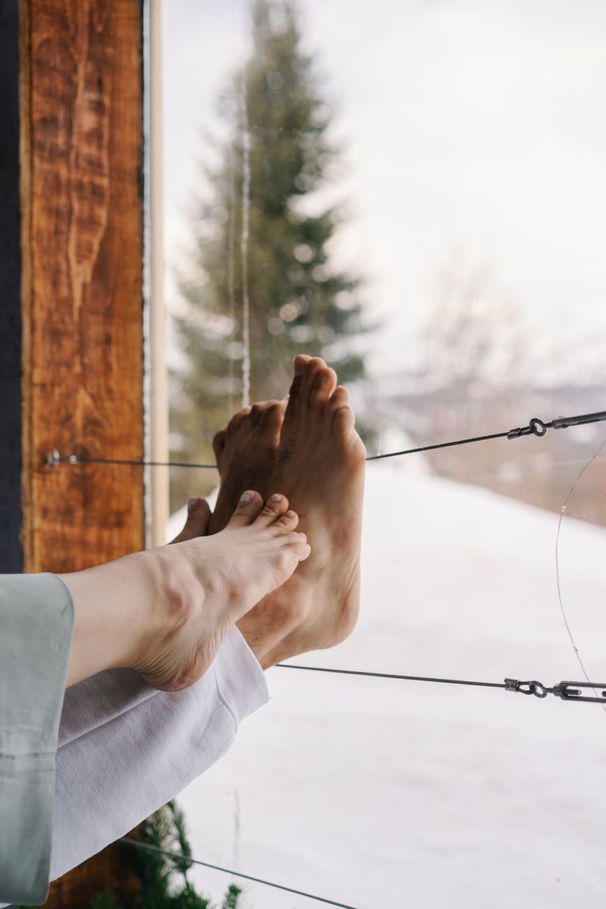 Relaxing indoors with a snowy mountain view, feet resting on a window ledge.