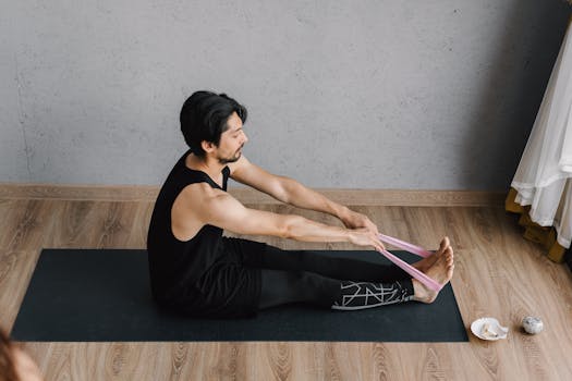 Man in black tank top performs yoga stretches with resistance band indoors.