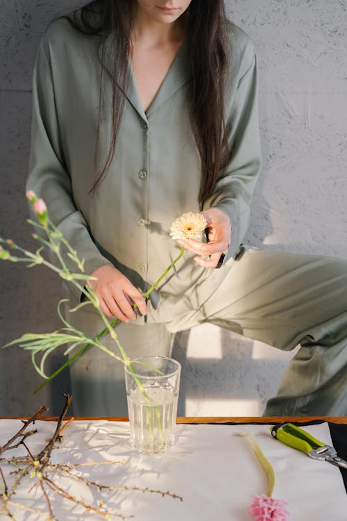 A Woman in Gray Pajama Arranging Flowers on a Glass with Water