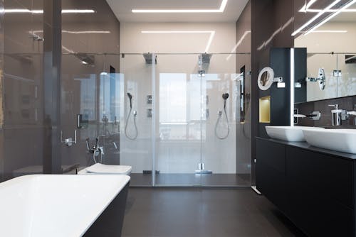 Interior of contemporary master bathroom with bathtub and shower cabin near wooden cupboards with ceramic sinks in modern apartment