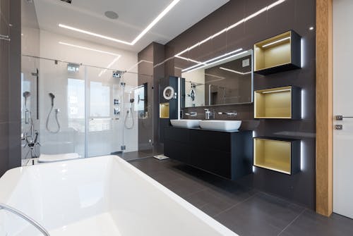 Interior of contemporary bathroom with glass shower cabin and ceramic bathtub in front of shelves hanging near sinks and mirrors