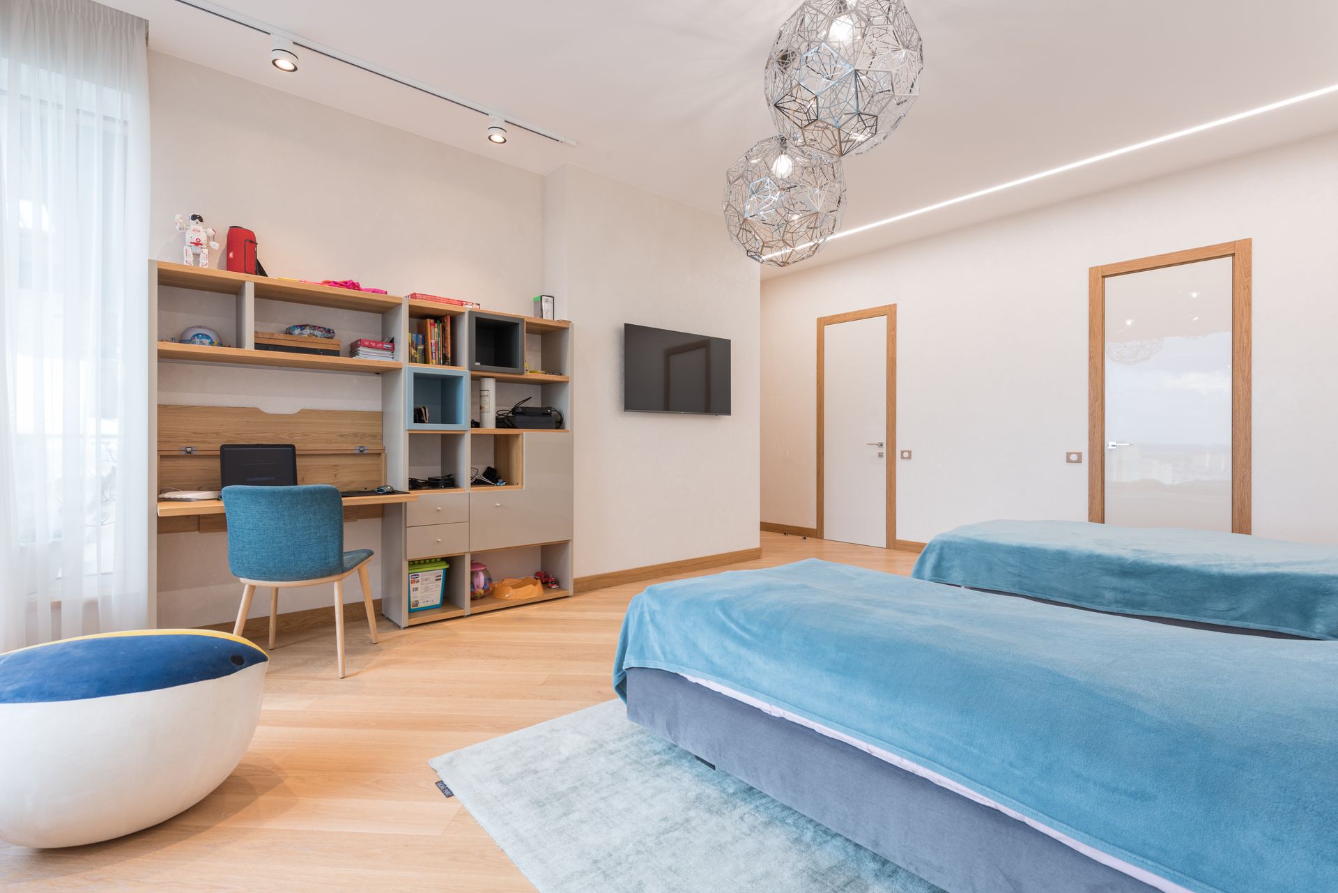Interior of modern bedroom with cozy beds and chair placed near wooden desk and bookshelf in contemporary apartment