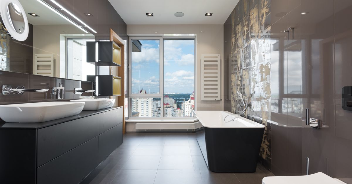 Wooden furniture with bathtub and ceramic sinks and toilet bowl in contemporary master bathroom with big windows in daylight