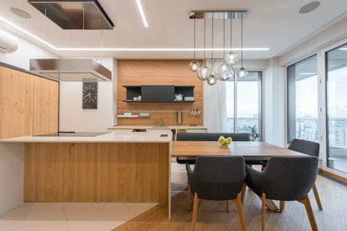 Interior of contemporary large clean kitchen with wooden cabinets and white counter under modern lights in apartment