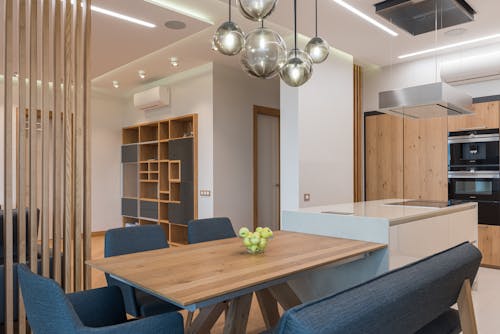 Brown table surrounded with blue chairs in dining room with modern interior and timber shelves