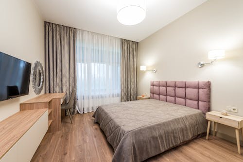 Contemporary bedroom with TV and curtains decorating window under bright luminous round shaped lamps