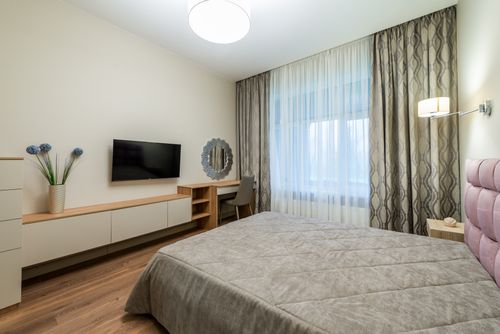 Free Interior of bedroom with soft coverlet placed opposite TV hanging near vase of flowers Stock Photo