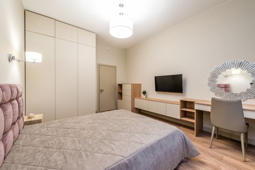 Free Interior of bedroom with comfortable bed under blanket placed near closet with TV set hanging on wall near mirror under lamp Stock Photo