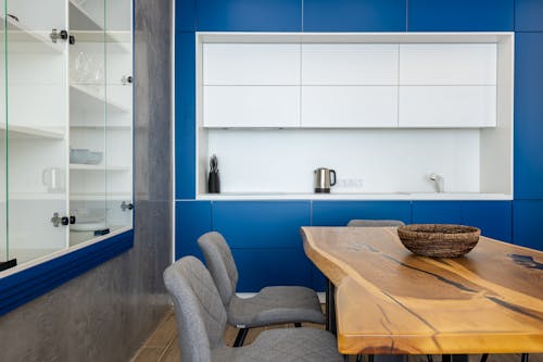 Stylish cupboards hanging on wall in modern kitchen with chairs placed around wooden table with wicker bowl