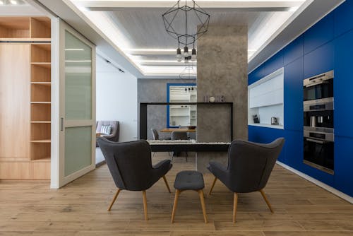 Interior design of contemporary kitchen with comfortable armchairs and blue cupboards with appliances under shiny ceiling illumination