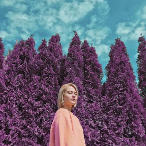 Woman in Pink Long Sleeve Shirt Standing In Front of Purple Trees