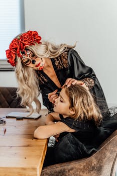 A woman and child in artistic Day of the Dead makeup indoors, preparing for Halloween.