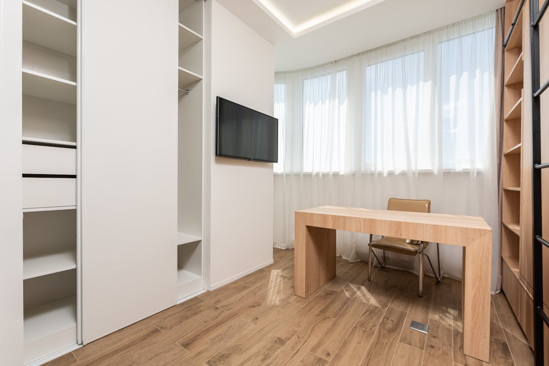 Free Chair At Wooden Table Near Wall With Window And Tv Between Opened Empty Wardrobes In Spacious Room With Minimalist Interior Stock Photo