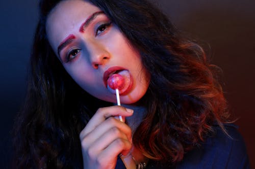 Woman in Blue Top Licking Pink Lollipop Candy Low-light Photography