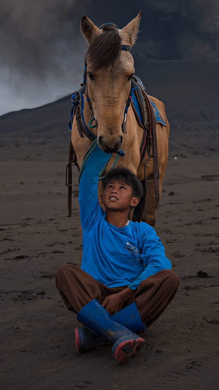 Ethnic Boy Caressing Horse In Desert In Twilight