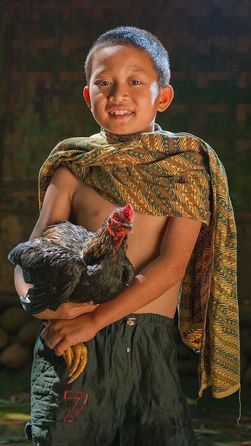 Cheerful Asian child in plaid holding black chicken while looking at camera on blurred background