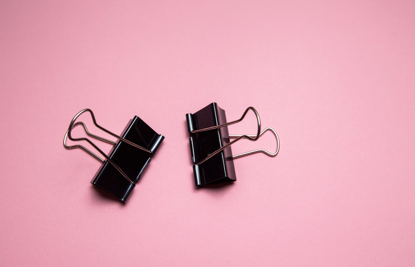 Two black binder clips on a pink background, showcasing a minimalist and modern style.