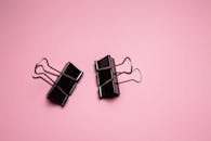Black paper clamps scattered on pink surface