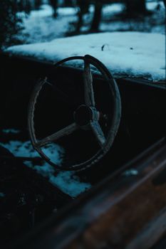 A rustic vintage steering wheel of an old car in a snowy, winter landscape.