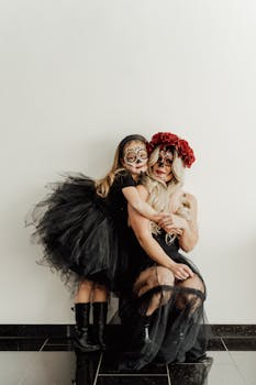 A mother and daughter embrace in artistic Halloween costumes and makeup against a white background.