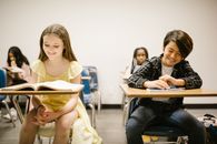 Two Students Smiling While Sitting on Their Desk