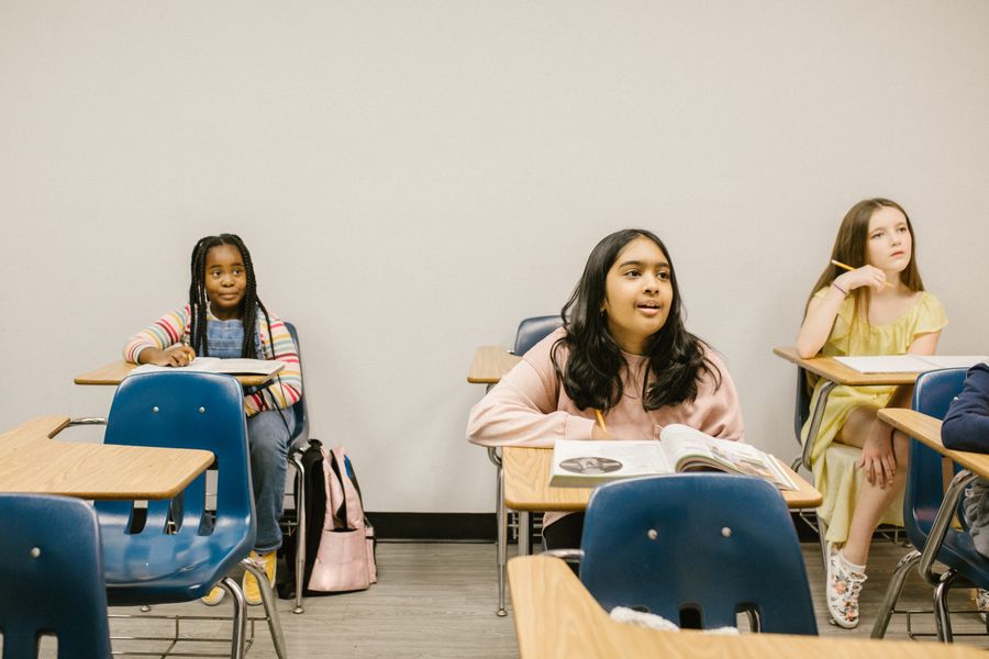 Three diverse students sitting in a classroom, engaged in learning.