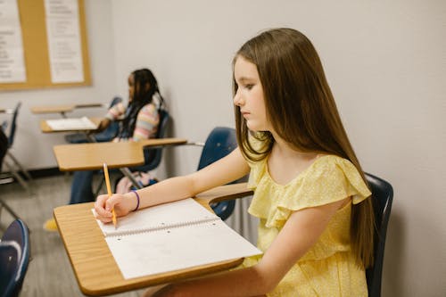 Free Girl Sitting on Her Desk Looking Lonely While Writing Notes on Her Notebook Stock Photo