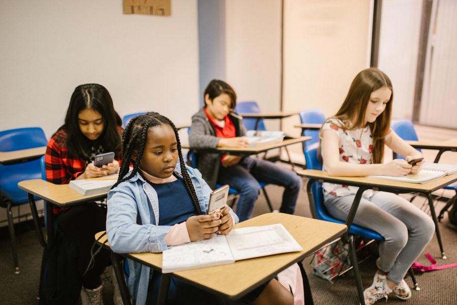 A group of students in a classroom looking at smartphones instead of their work