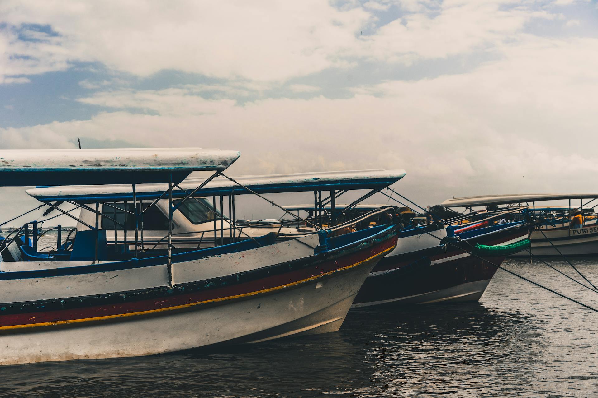 Traditional fishing boats docked at a serene harbor in Bali, Indonesia, under a cloudy sky.