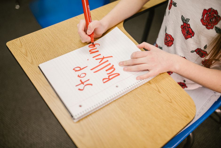 子供が学校の机のノートに「いじめをやめよう」と書き、意識向上を図っています。