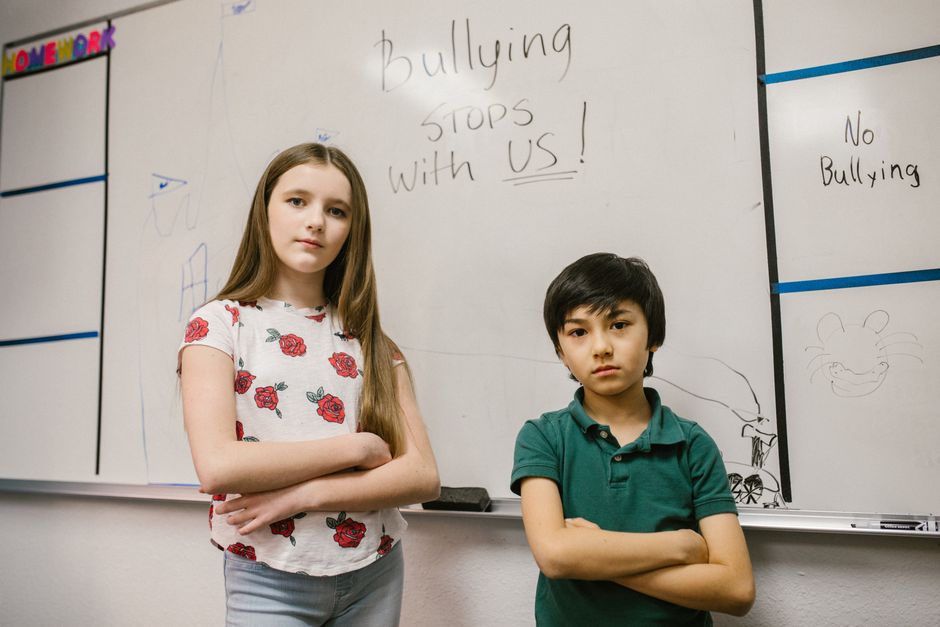 教室のホワイトボードの前で、自信を持って立っている二人の子供、いじめ防止のメッセージが描かれています。