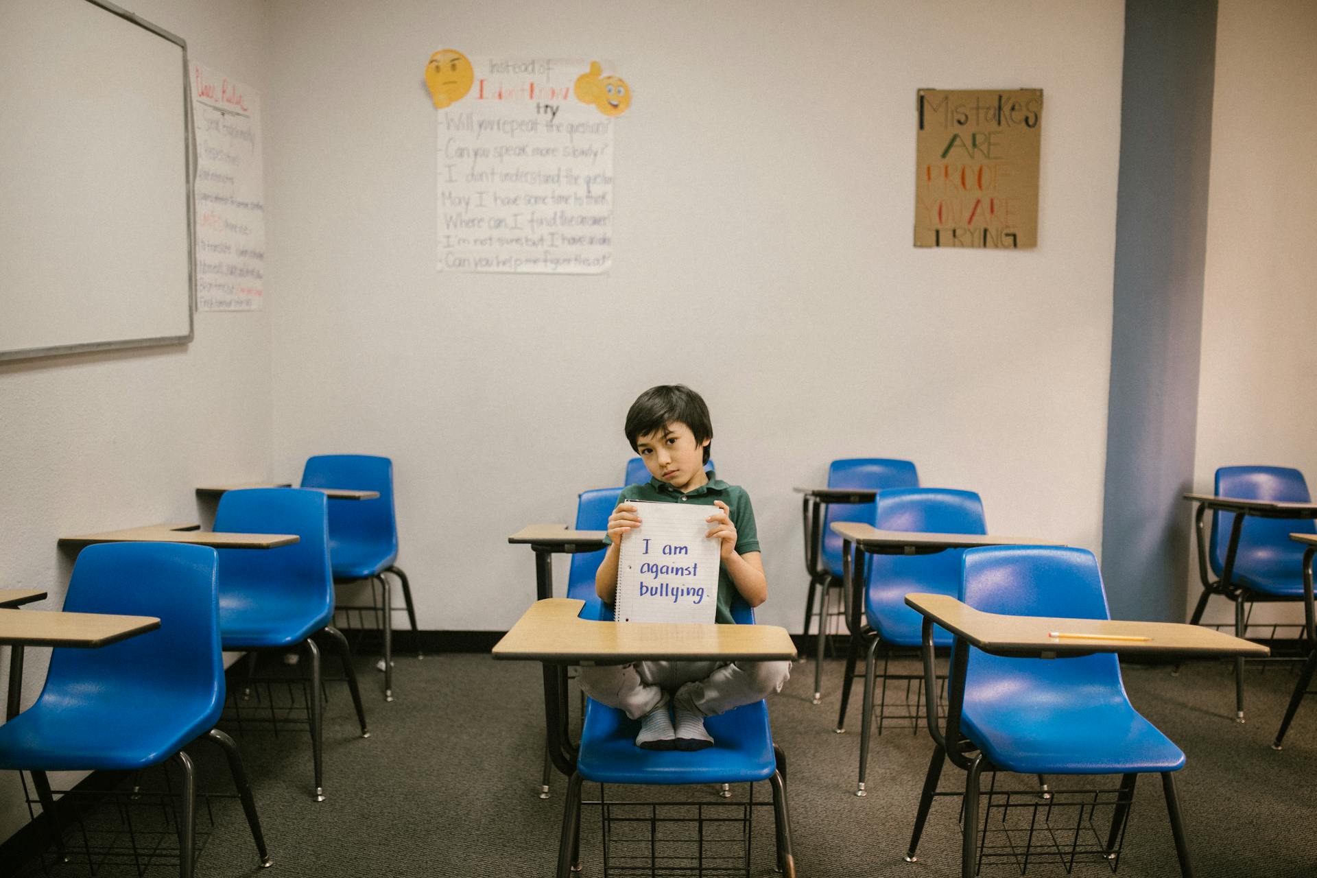 Boy Sitting on Blue Chair While Holding a Message Against Bullying