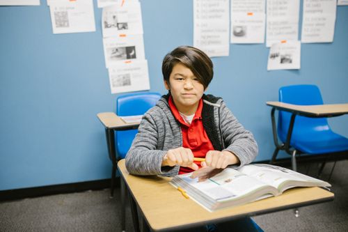 Free Young student sitting confidently at a desk in a classroom with books. Stock Photo