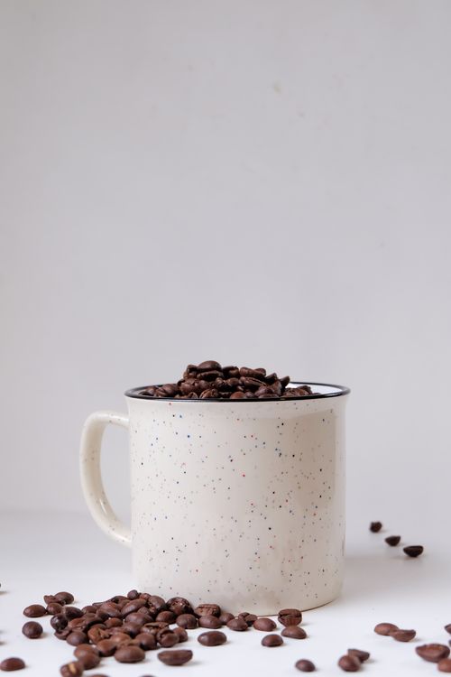 Free A speckled ceramic cup filled with roasted coffee beans against a white background, emphasizing simplicity. Stock Photo