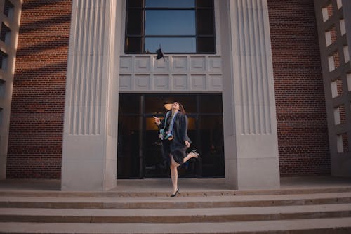 A Happy Woman Wearing Black Toga Standing Outside the University Building