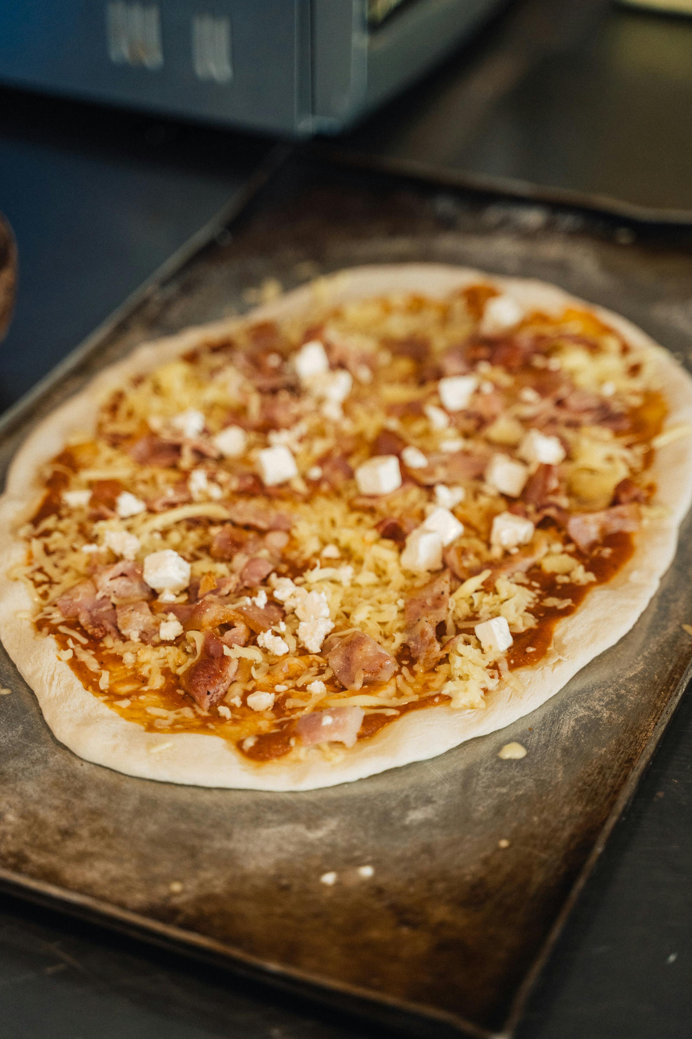 Close-up of a delicious homemade pizza with cheese and meat toppings on a baking tray.