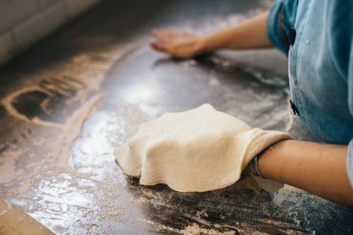 Free Close-up of a worker in a blue shirt kneading dough on a floured work table in a pizza parlor. Stock Photo