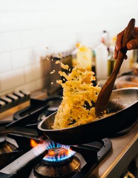 Close-up of chef skillfully tossing fried rice in a pan over a lit stove.