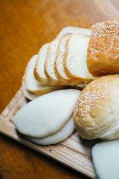 Close-up of various bread types including sliced white bread and sesame buns on a wooden board.