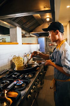 Professional chef tossing fried rice in a commercial kitchen with a stovetop and wok.